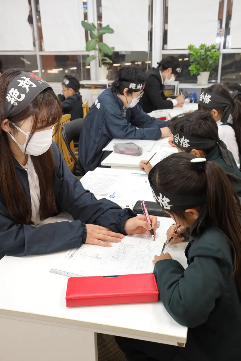 塾のプロ講師が生徒に志望校合格のための受験勉強のポイントを個別指導しているシーン
